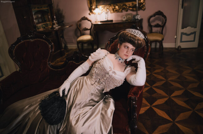 Grimilde Malatesta in Palazzo Facchi during a Historical Reverie event, photographed by Agnese Morganti. She's wearing her pearl butterfly edwardian dress, while leaning on a sofa.